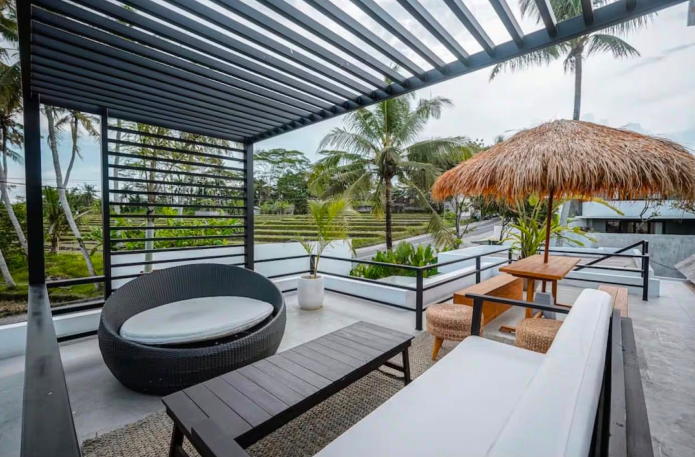 Rooftop terrace under a pergola looking over rice fields and coconut palms