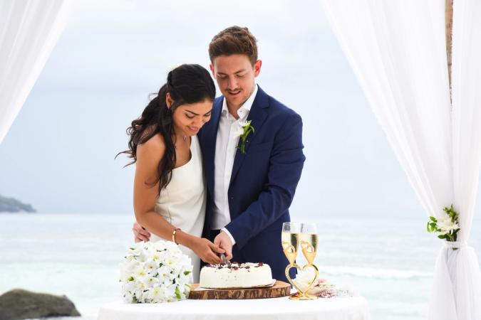 A couple in wedding attire slicing a cake together