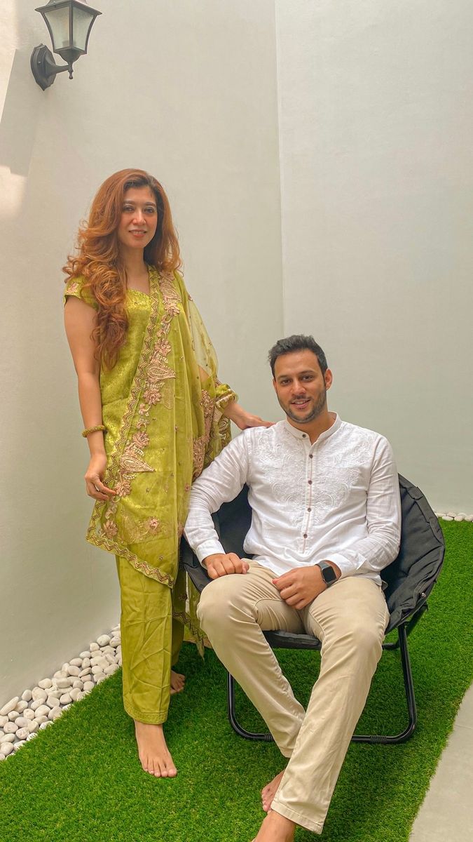 A woman in Indian attire standing beside a man sitting in a chair