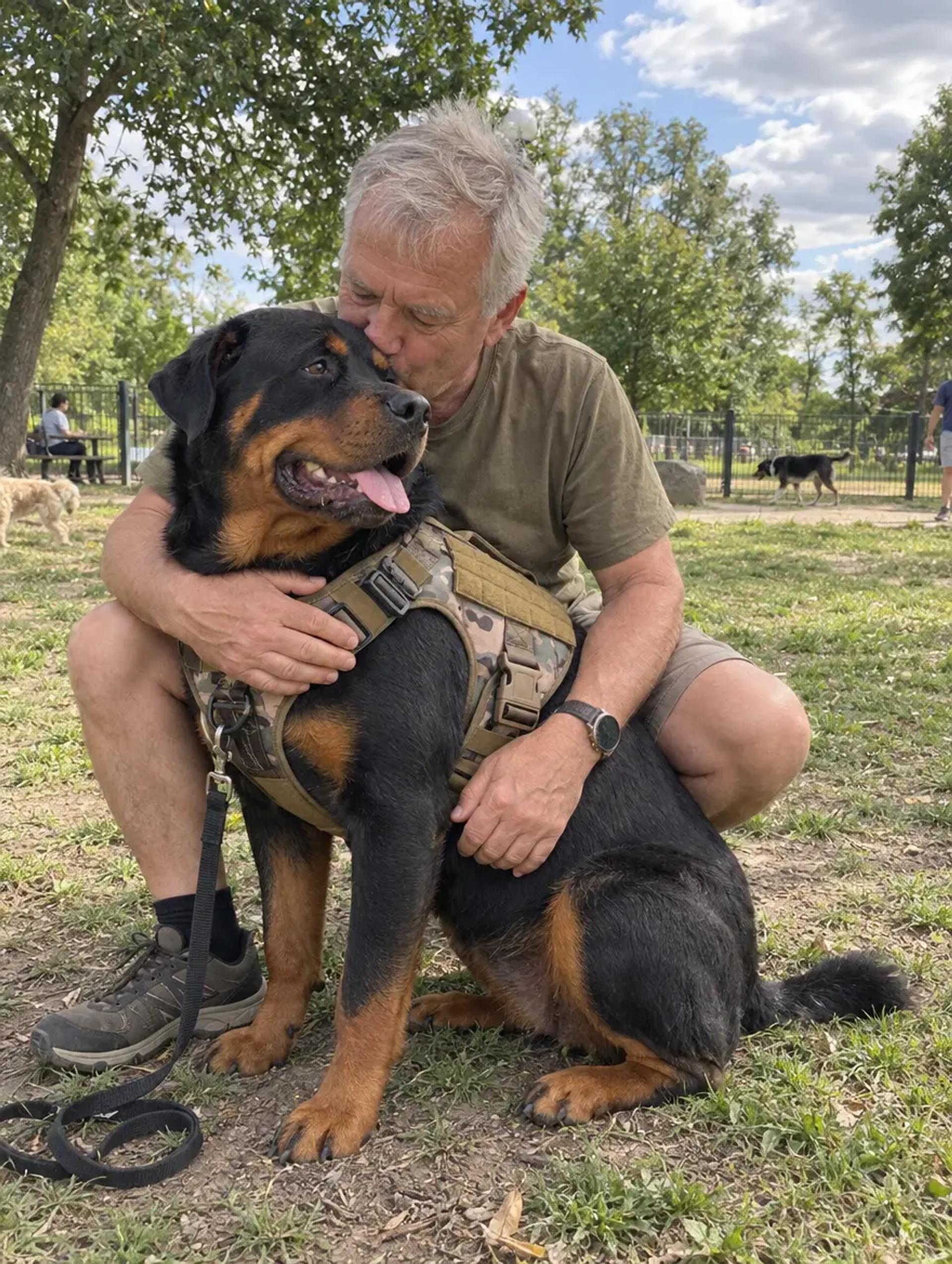 Man hugging his Rottweiler in a camo Tactical Harness at the dog park
