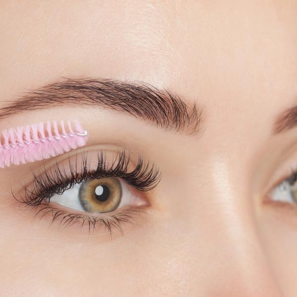 Nærbilde av vipper og bryn på kvinne som holder en mascarabørste
