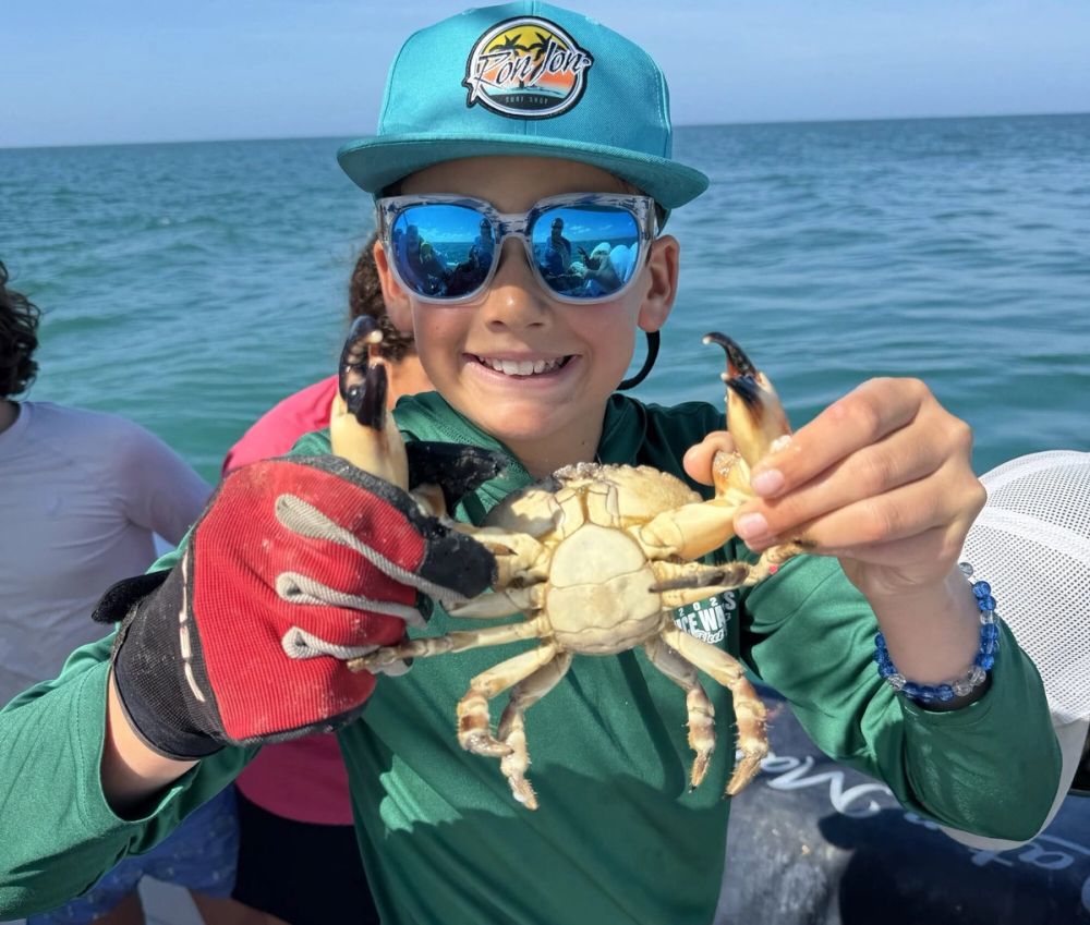 A student holds up a crab aboard a boat during marine science fieldwork.