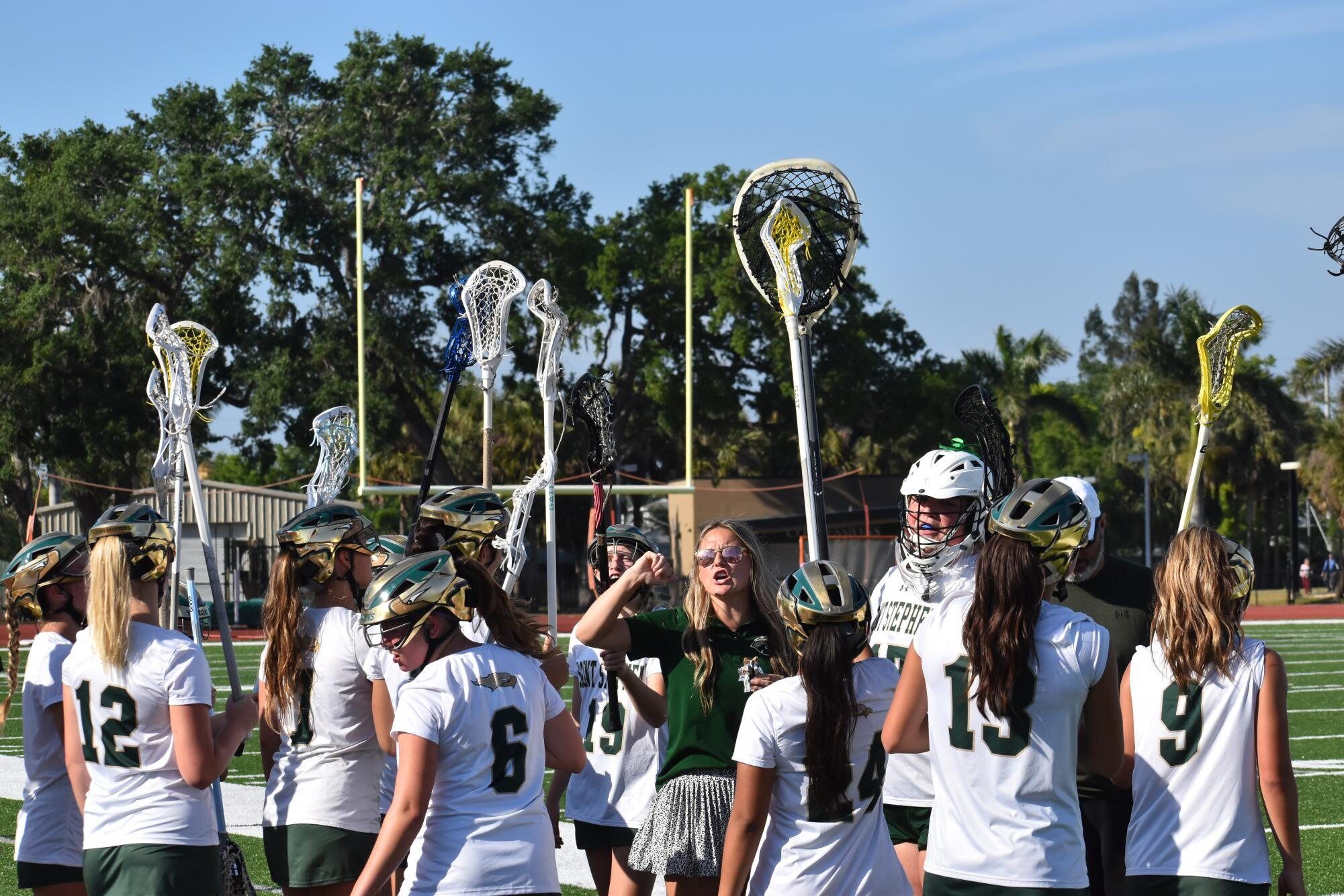 The girls' lacrosse team raises their sticks and cheers together before a game.