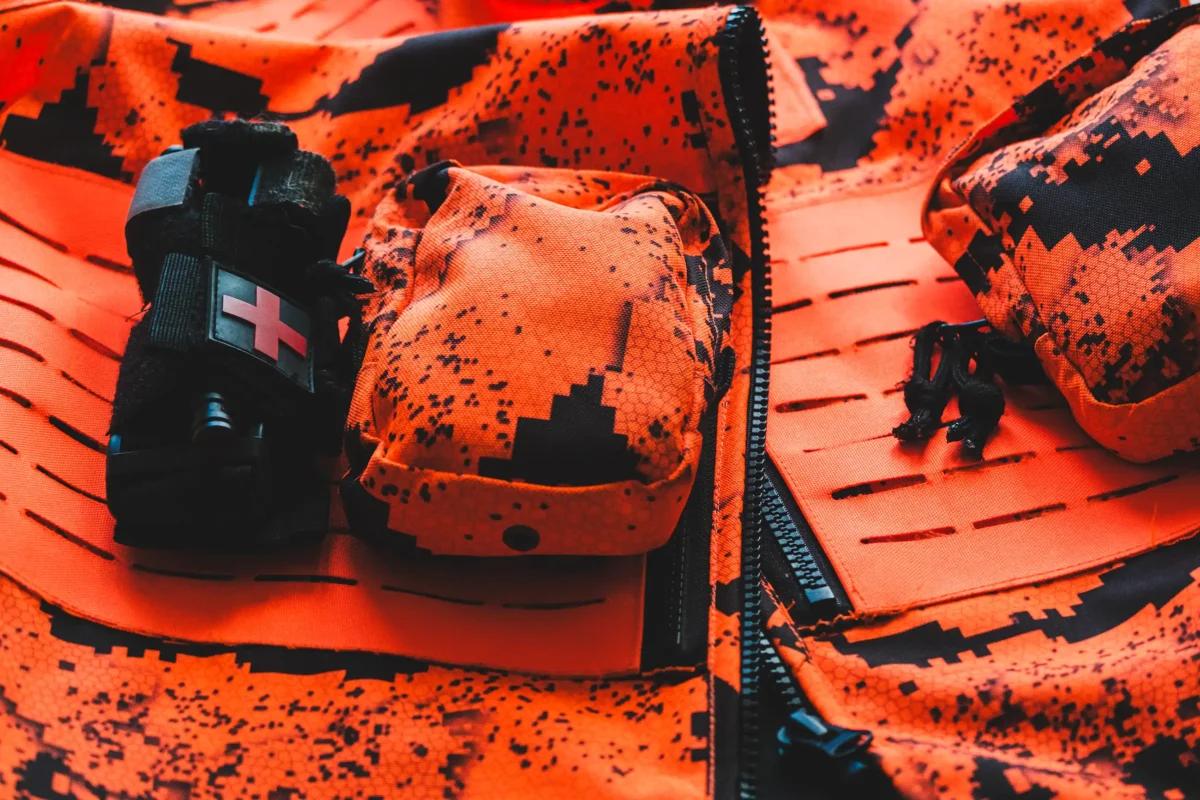 Oranssi maastokuvioinen metsästysliivi ja ensiaputasku