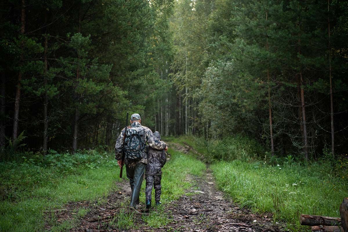 Aikuinen ja lapsi maastovaatteissa kävelemässä metsätietä pitkin