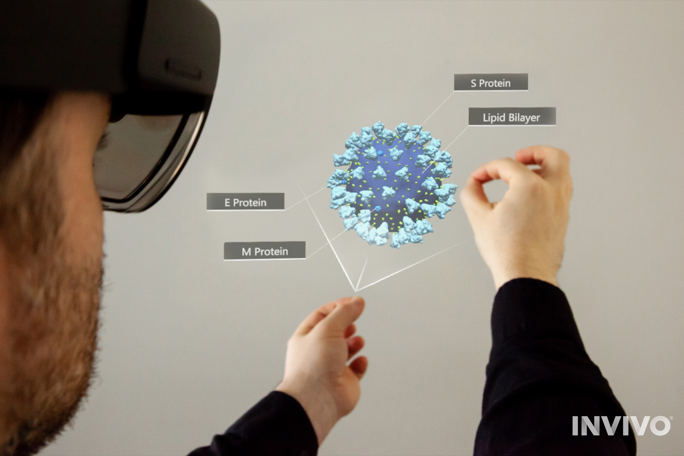 Seen from an over-the-shoulder perspective, a person wearing a HoloLens 2 headset manipulates a coronavirus molecule. Labels and vectors are visible near their pinched fingers.