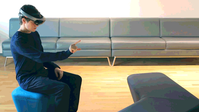 A person sitting down wearing the headset gestures, and manifests a small holographic figure, which then coughs.