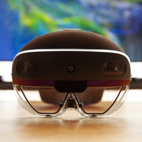 A HoloLens 2 headset from the front, resting on a table with blue and green art on the wall behind, blurred with the perspective.