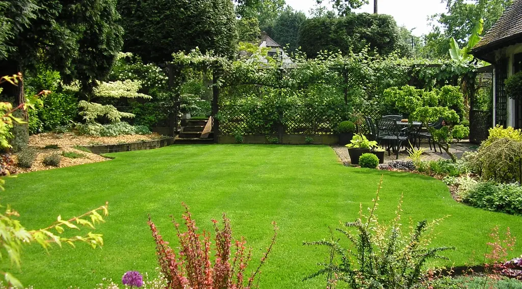 A well-kept garden with a lush green lawn, surrounding shrubs, and a patio seating area in the background.