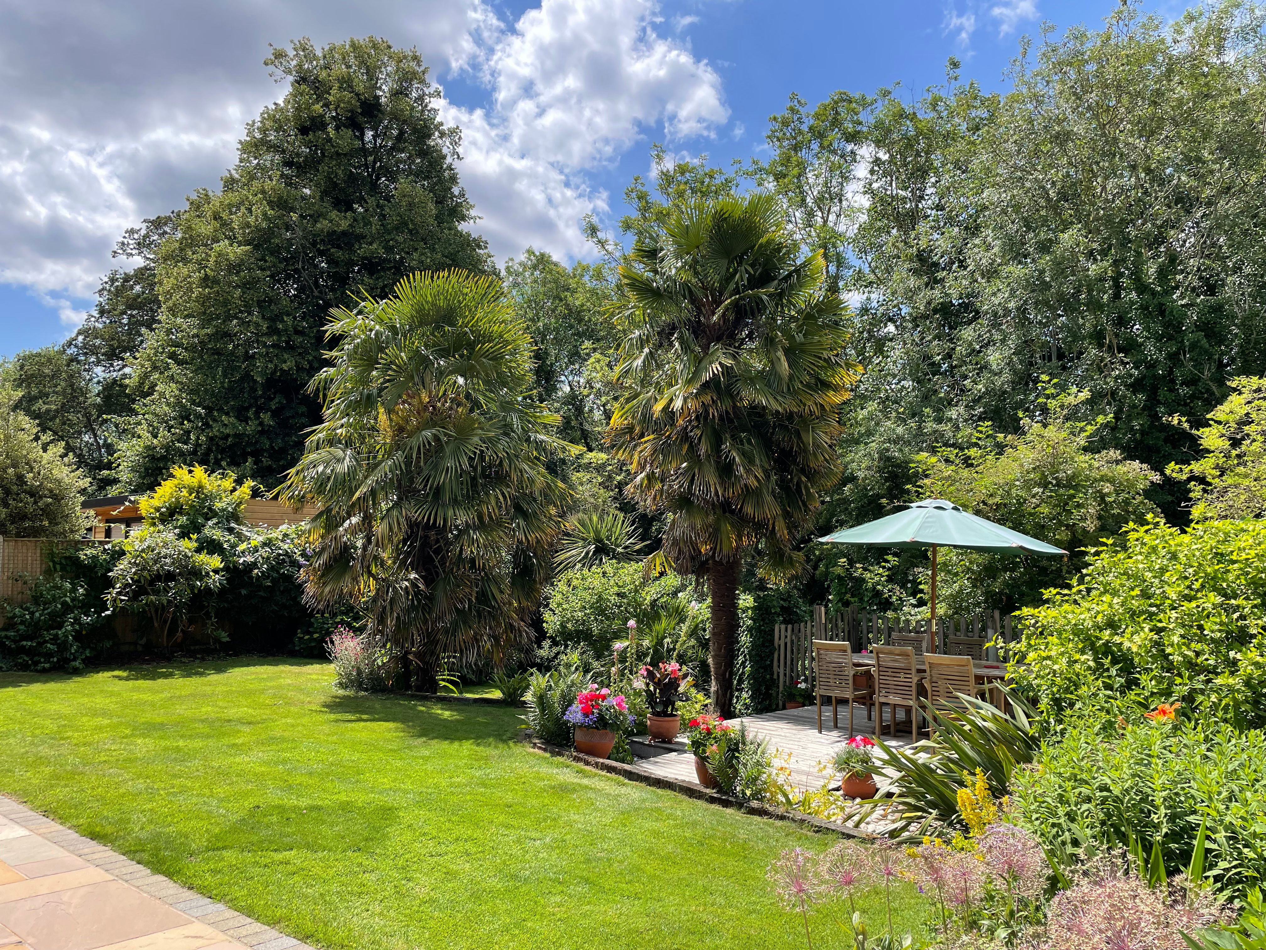 lush green lawn with a border of trees, plants, and flowers, with a beautiful seating area.