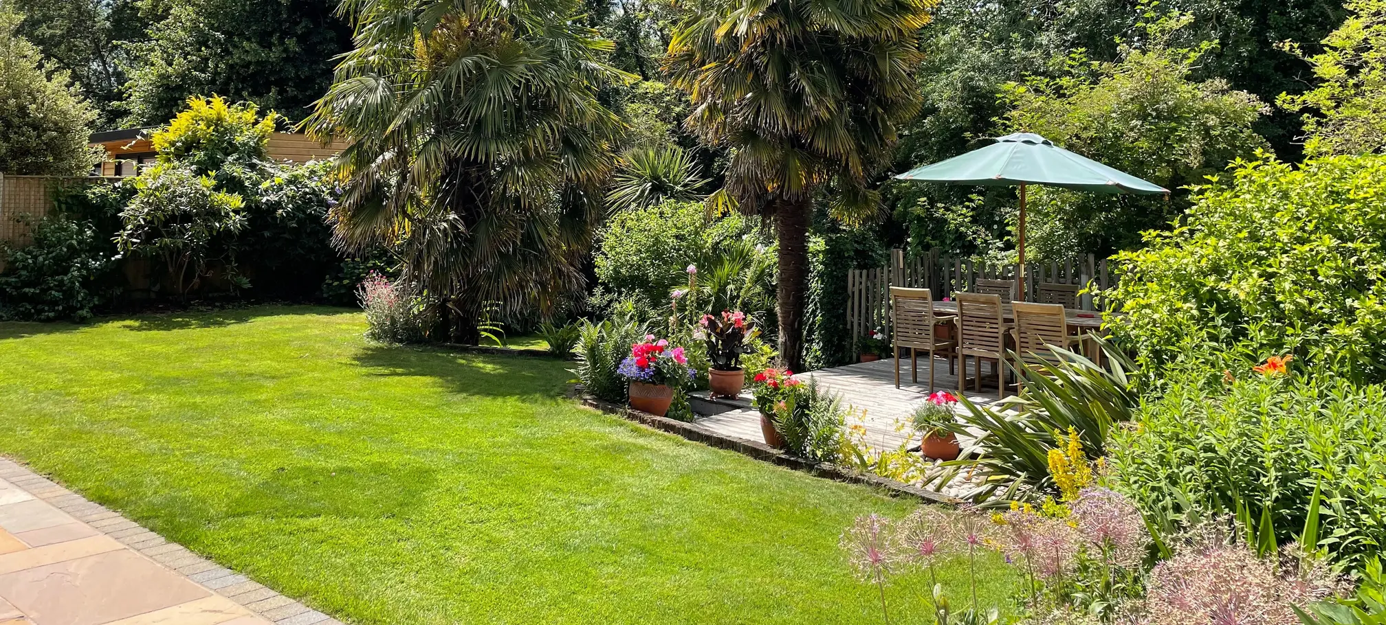 lush green lawn with a border of trees, plants, and flowers, with a beautiful seating area.