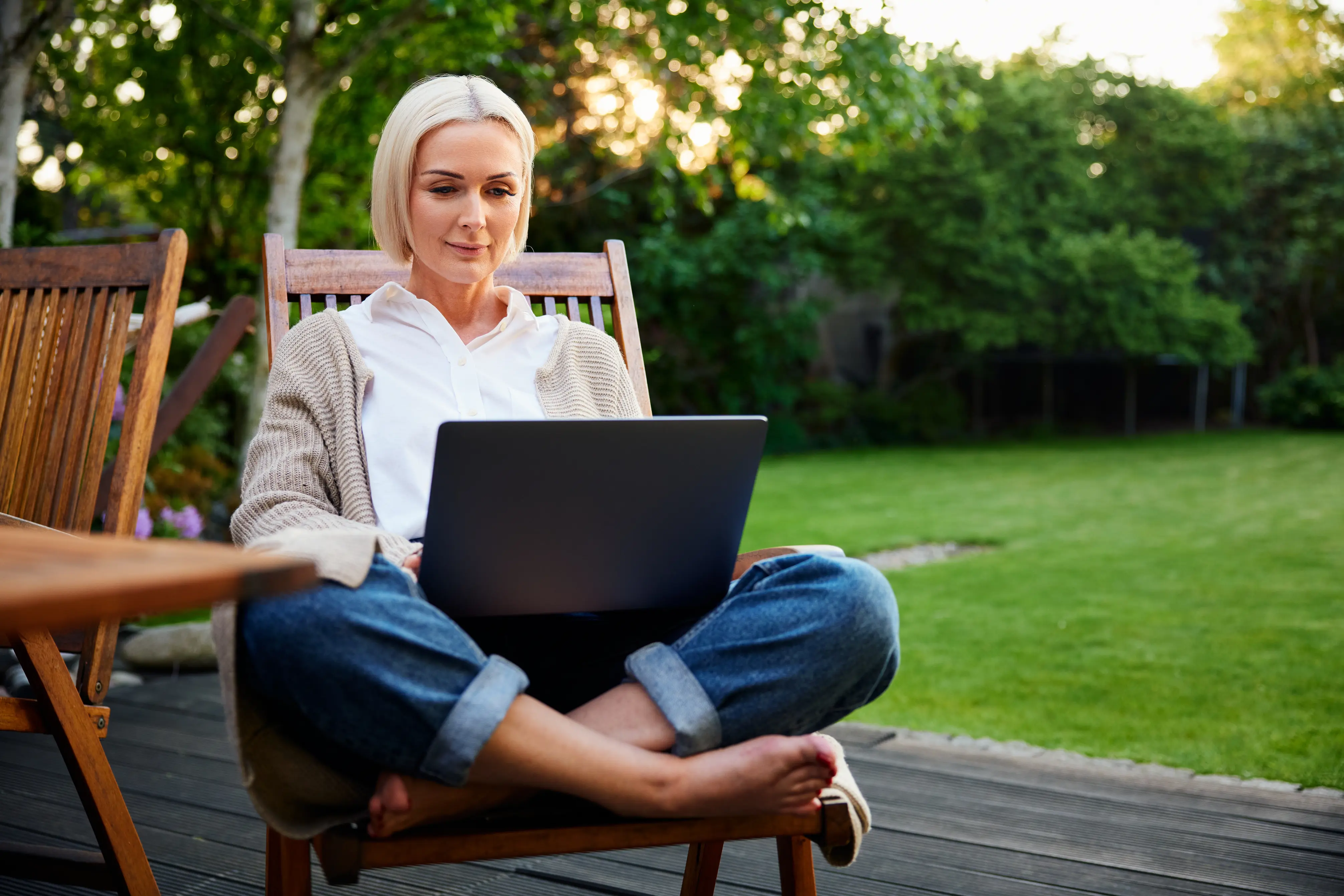 Women relaxing in the garden on her laptop, surrounded by a lush green lawn.