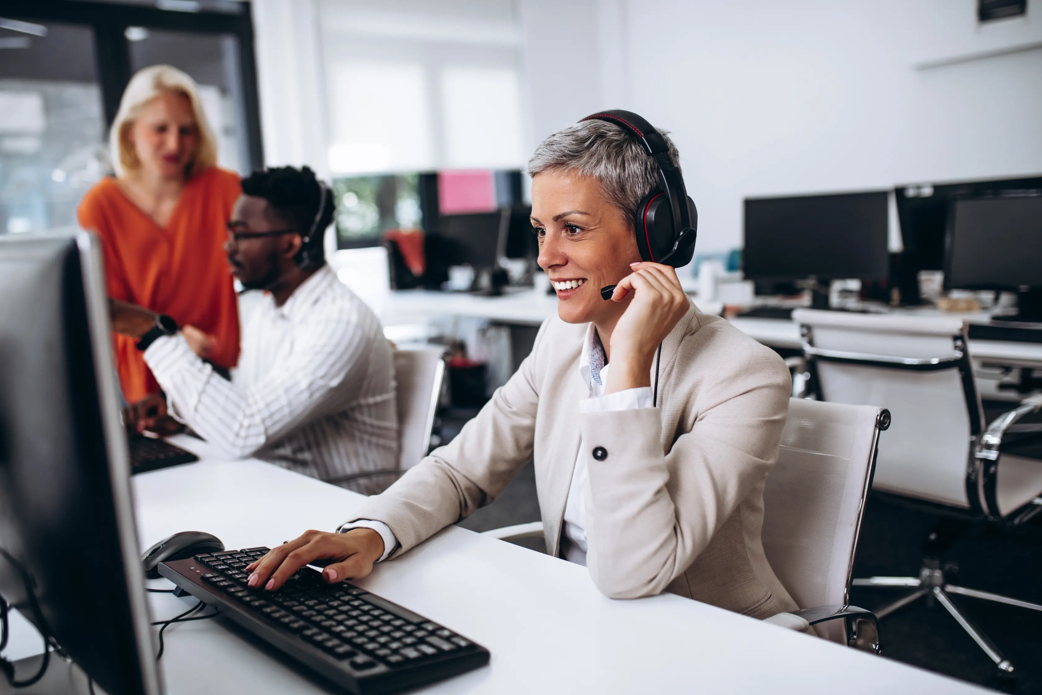 Customer service representative wearing a headset and speaking on a call at an office desk.