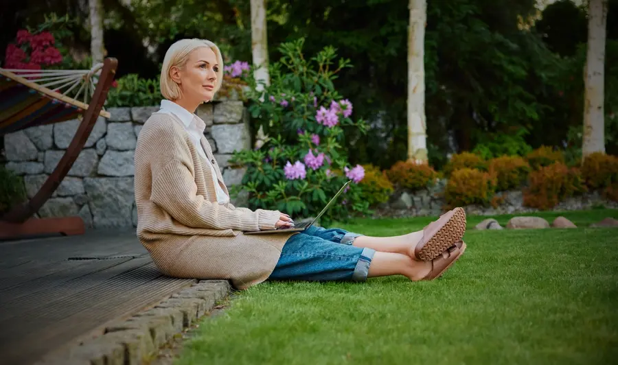 Woman relaxing on a garden deck with a tablet, overlooking a well-kept lawn and flowers.