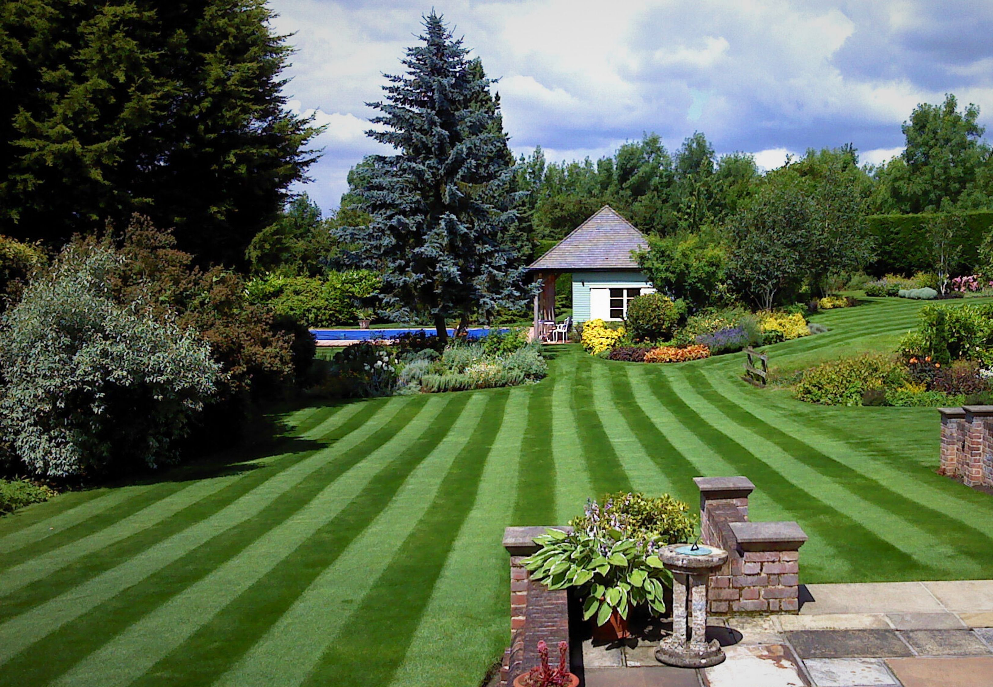 Beautiful striped lawn with lush green grass and garden borders, showcasing the results of GreenThumb professional lawn care.