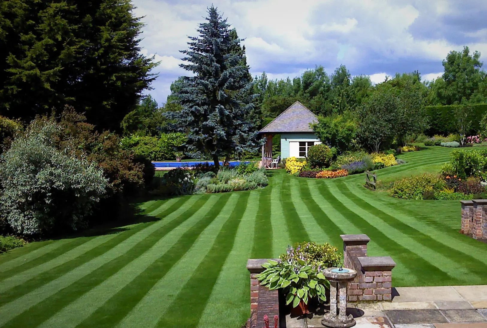 Beautiful striped lawn with lush green grass and garden borders, showcasing the results of GreenThumb professional lawn care.