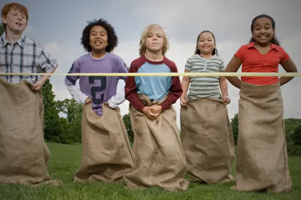 Kids enjoying a sack race on a sunny lawn during a backyard sports day.