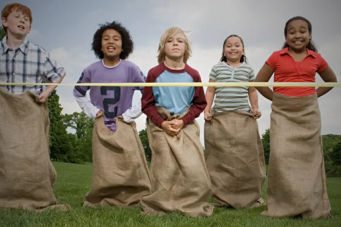 Kids enjoying a sack race on a sunny lawn during a backyard sports day.