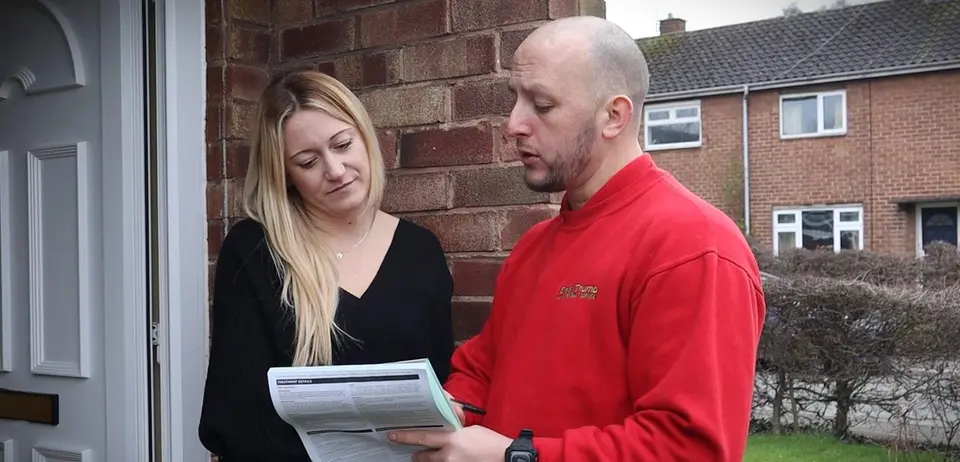 GreenThumb lawn specialist discussing a treatment plan with a customer outside her home, holding a printed Lawn Condition Report during a consultation visit.