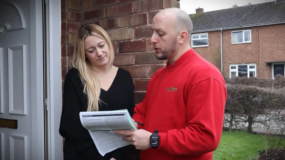 GreenThumb lawn care specialist explaining treatment details to a customer at her doorstep, holding an information sheet outside a suburban home.