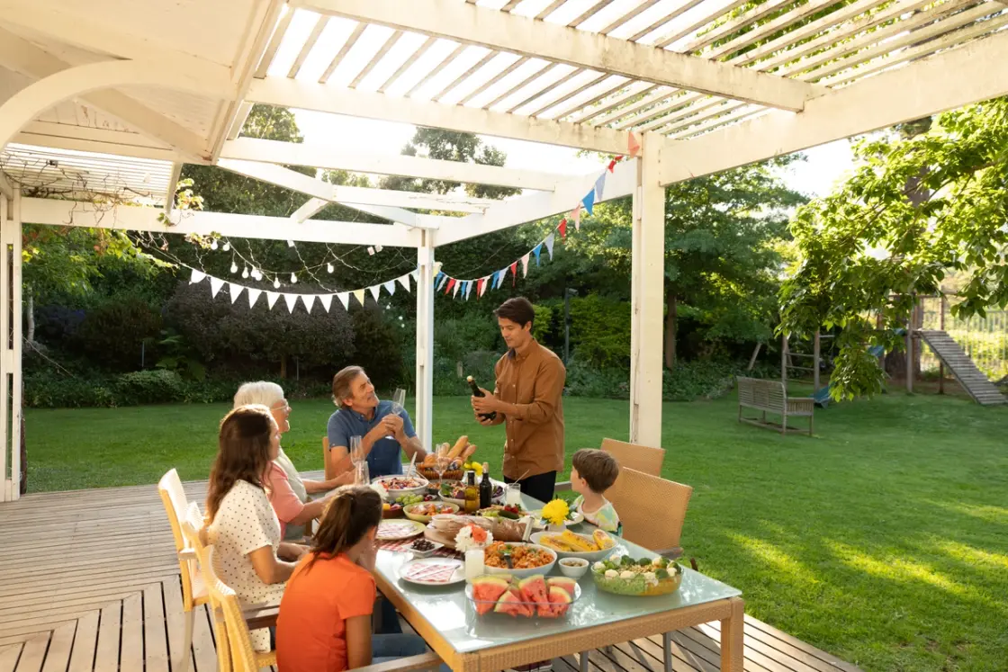 Family sitting around the table in the garden on a sunny day surrounded by lush green grass