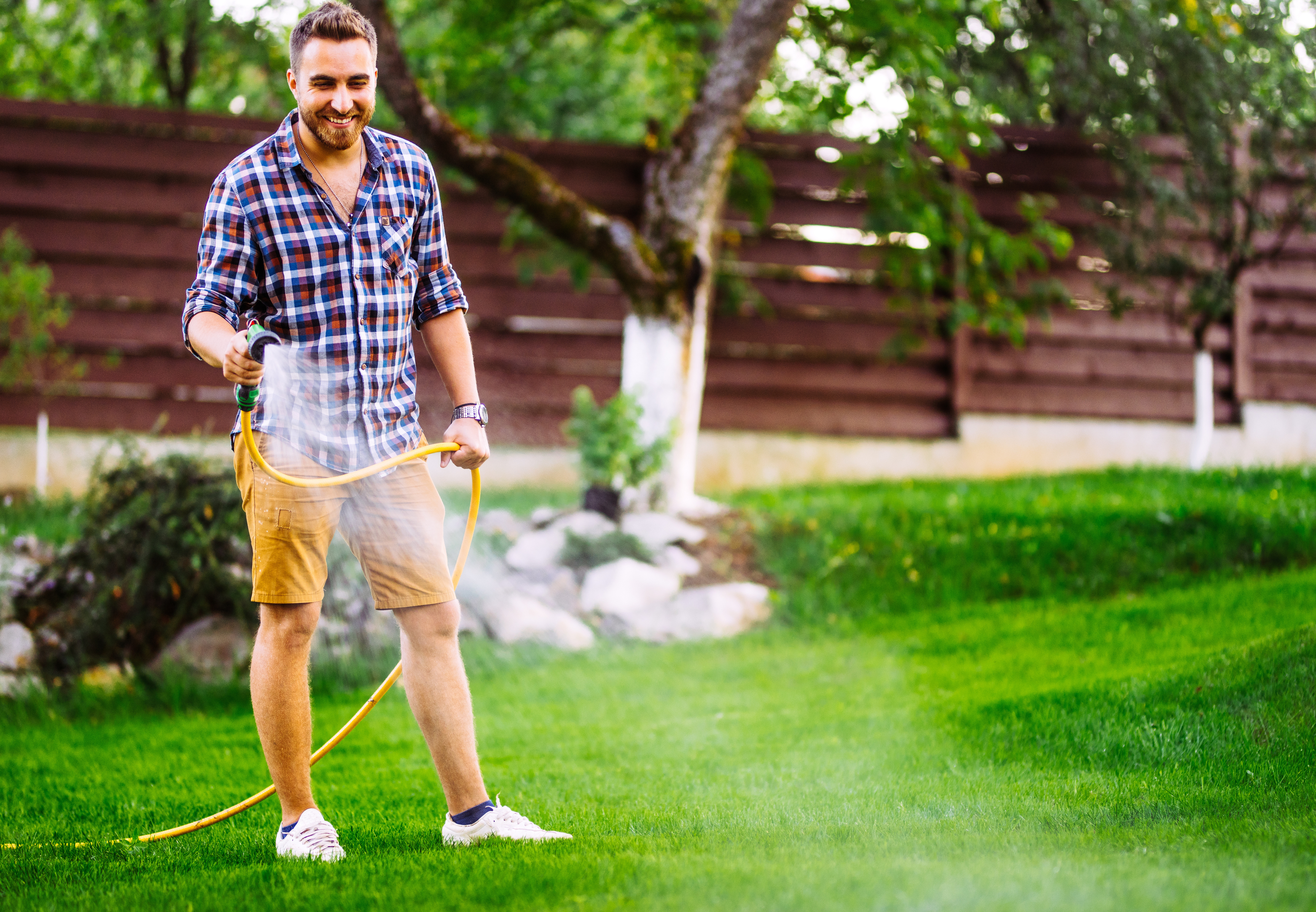 Man standing outside on his lawn, watering the grass with a hose.