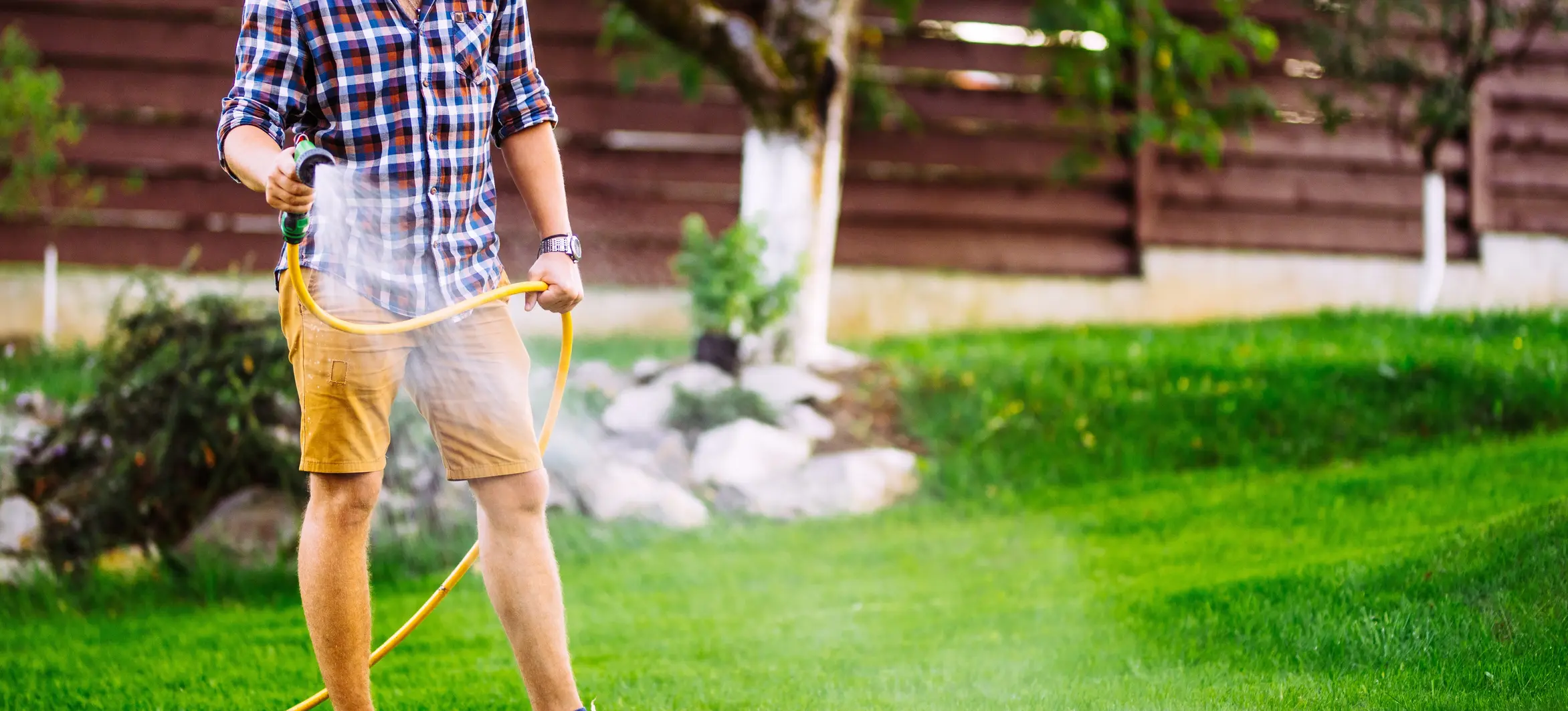 Man standing outside on his lawn, watering the grass with a hose.