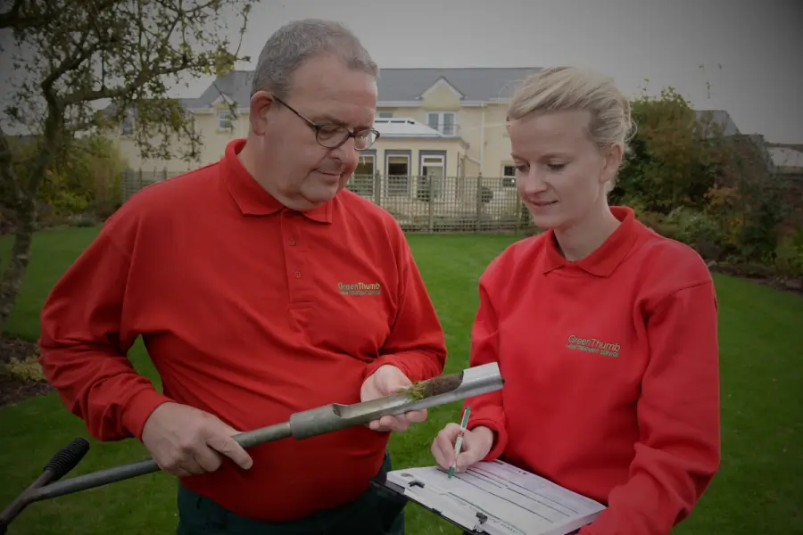 Two GreenThumb professionals analysing a core soil sample in a garden, assessing lawn health and planning treatment.
