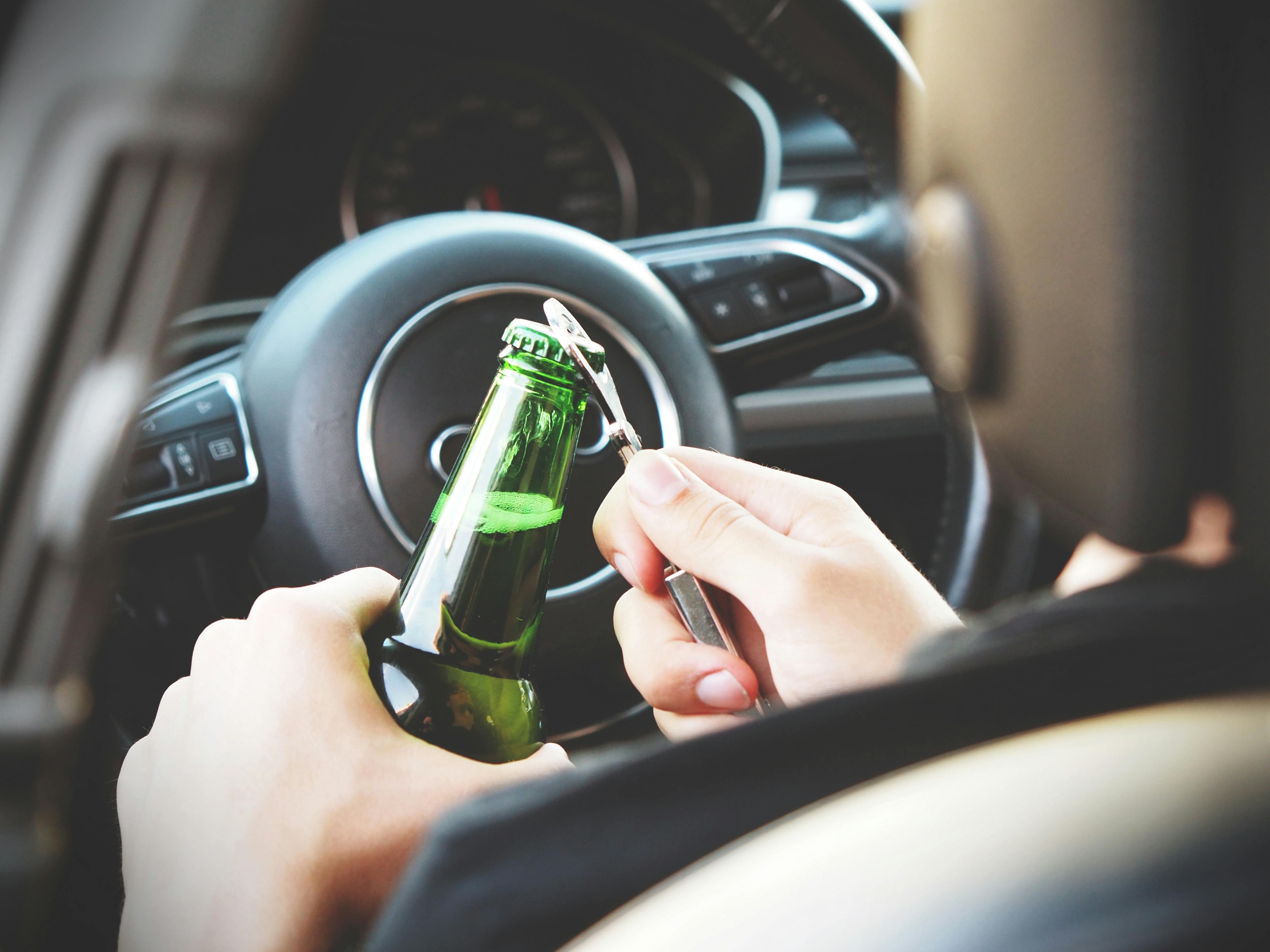 Image Driver opening a beer bottle behind the wheel, highlighting DUI laws in Palm Beach County