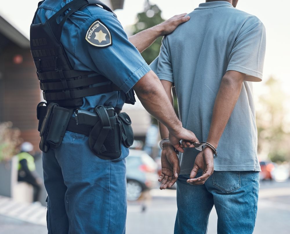Person in handcuffs being detained by a police officer during an arrest, illustrating the criminal process after being taken into custody