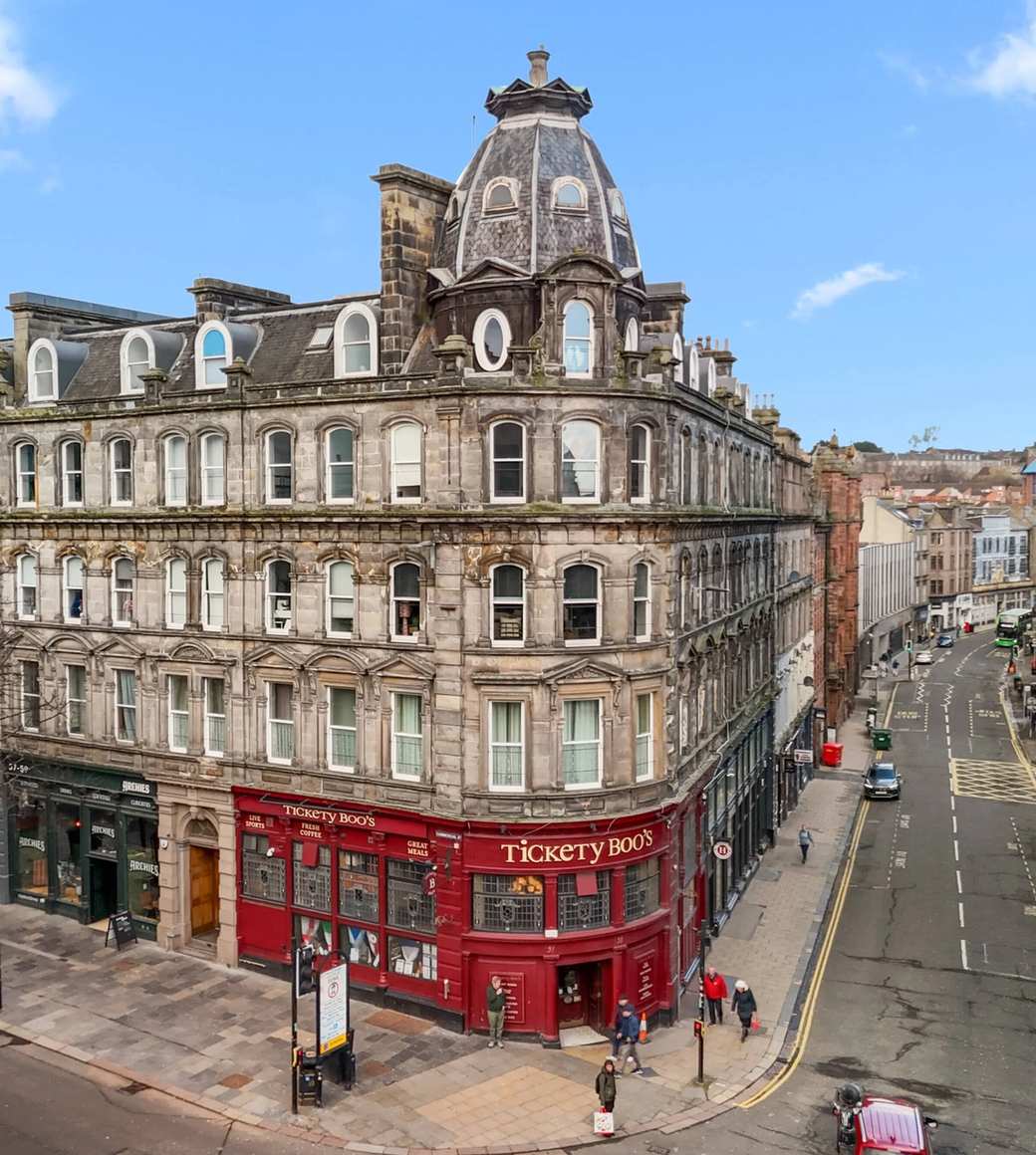 Historic stone building with mansard roof and cupola at a street corner in a British city centre, surrounded by Victorian architecture