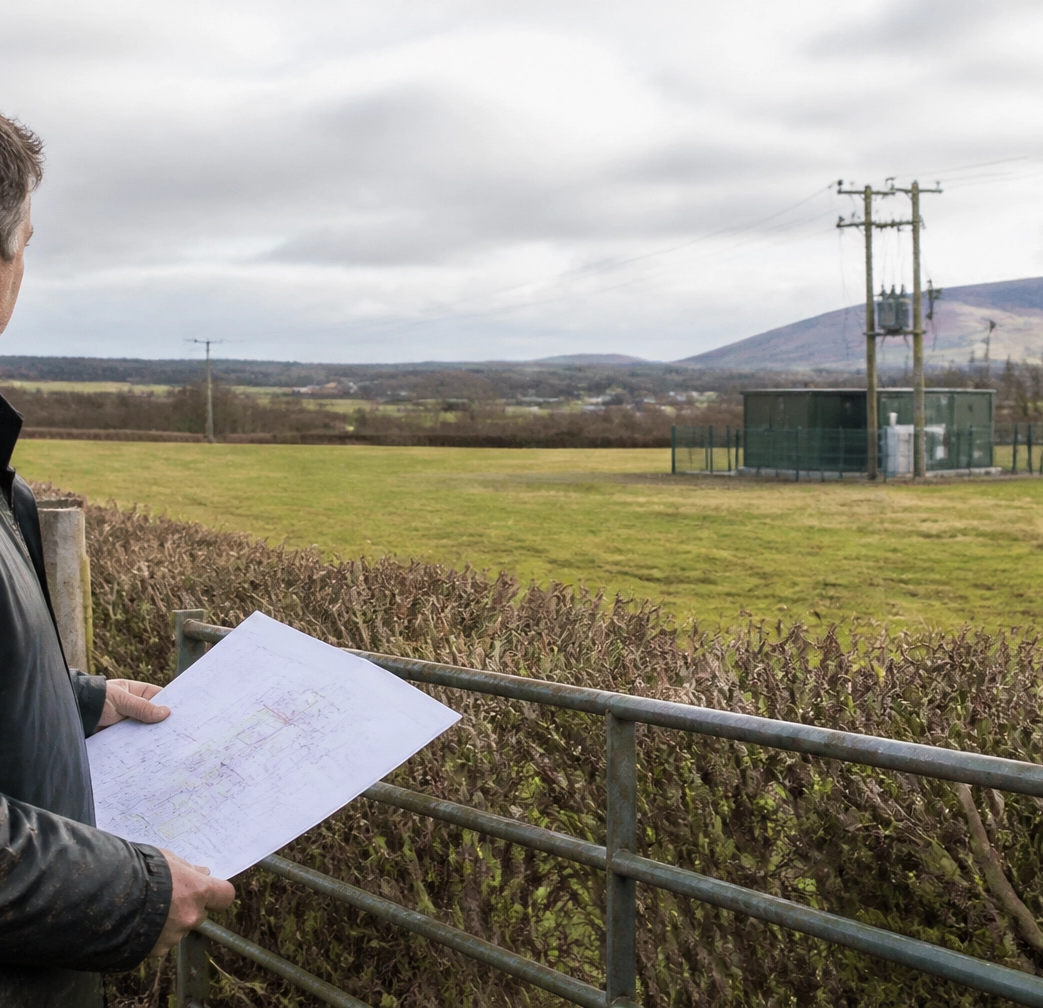 Farmer reviewing a potential solar farm site near rural grid infrastructure
