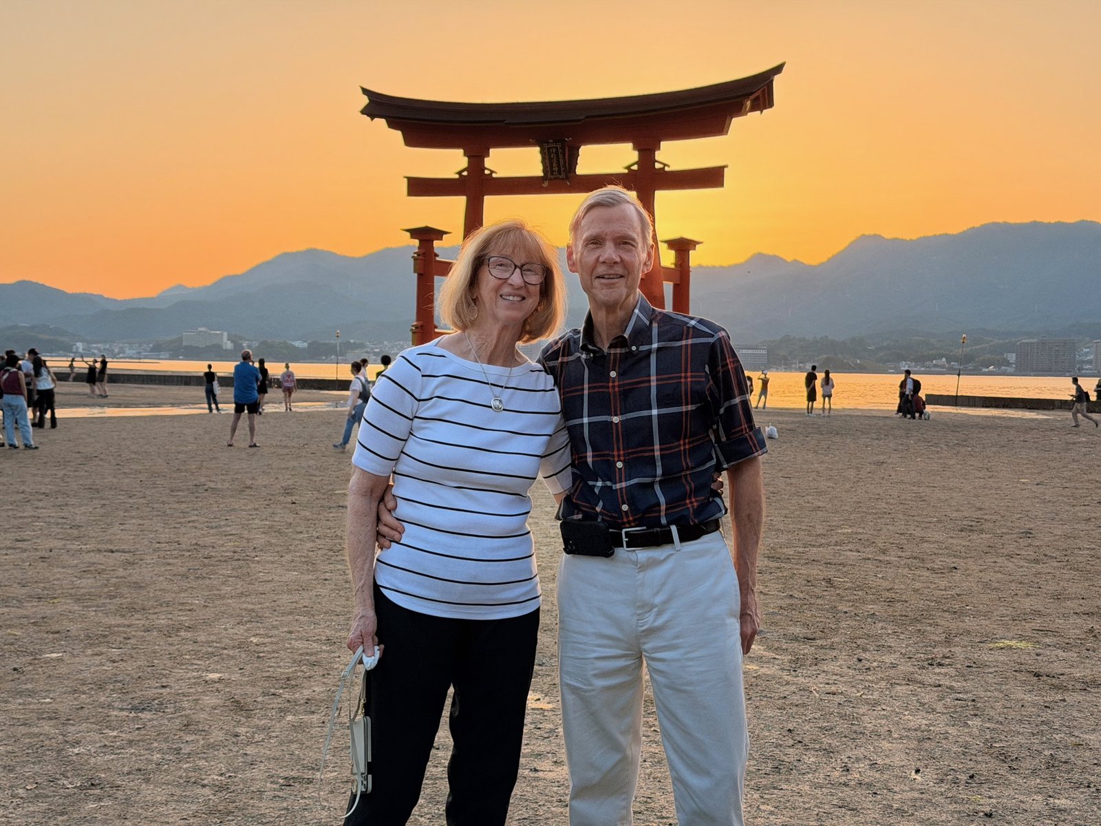 Two travelers smiling in front of the great torii with an orange sunset behind them.