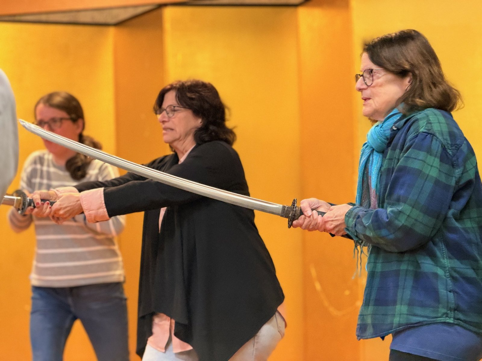 Three participants holding swords in front of a yellow folding screen.
