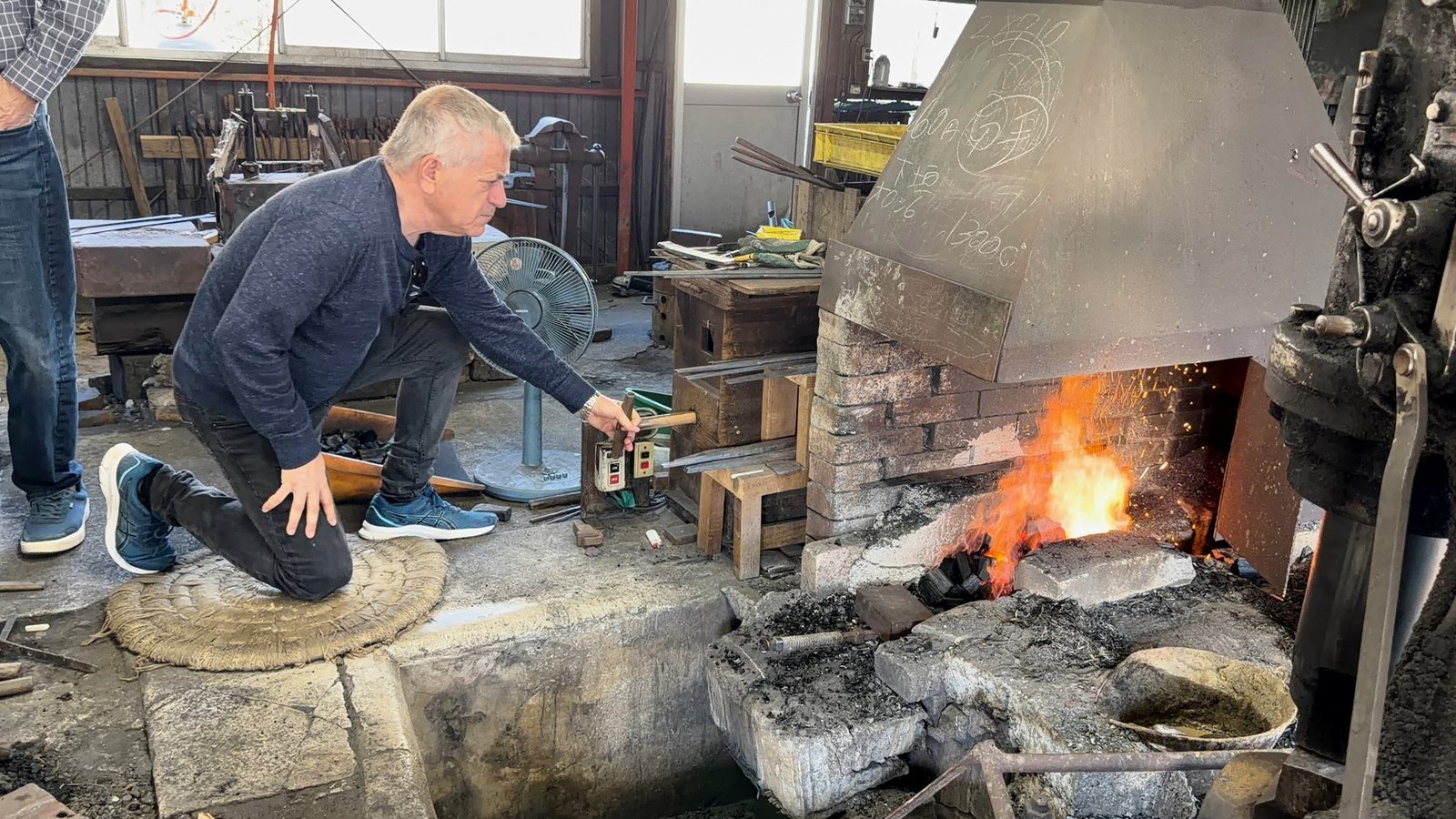 A participant kneeling beside a glowing forge, surrounded by workshop machinery and tools.