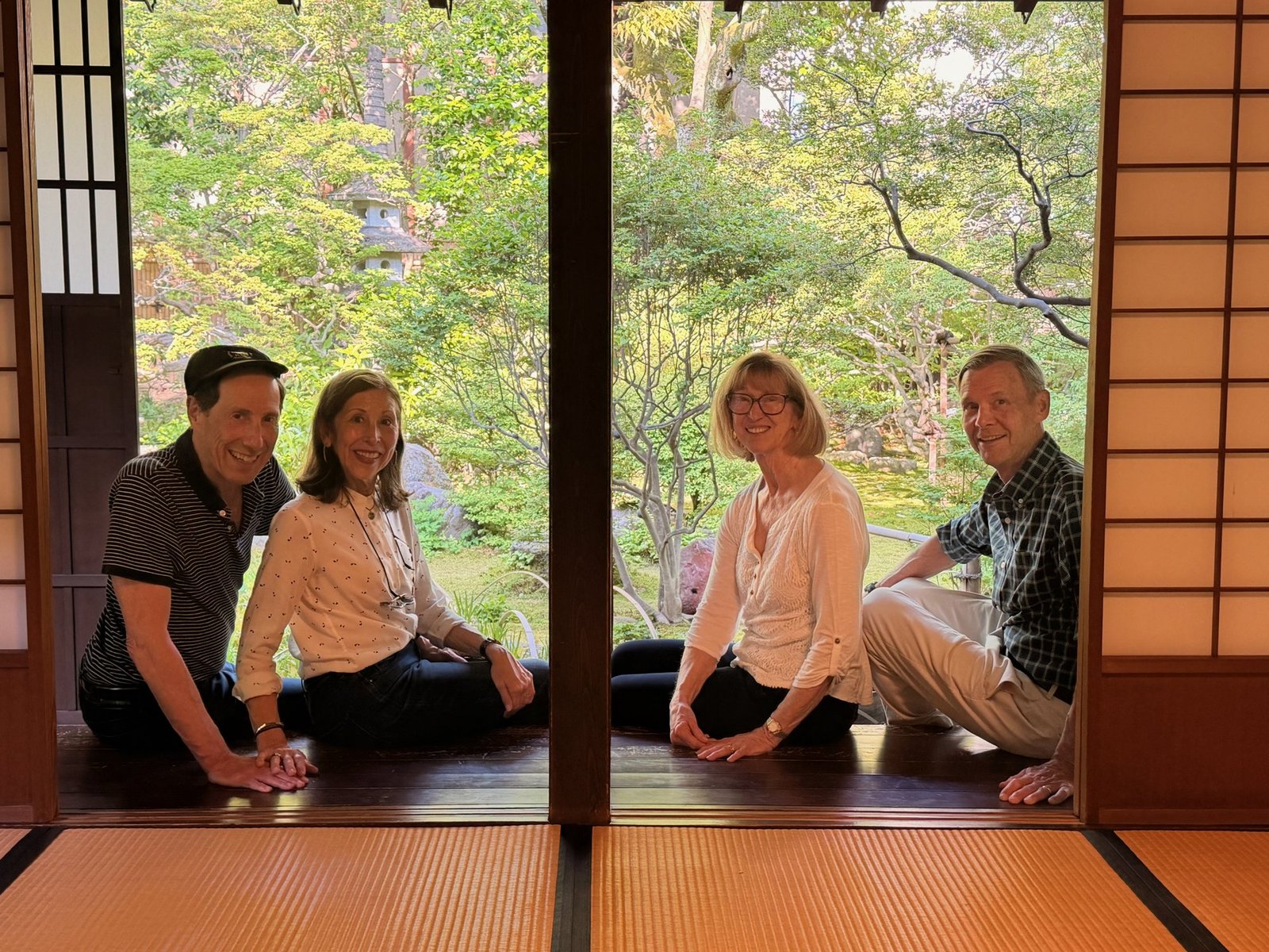 Four travelers seated in a traditional room beside an open view into a green garden.