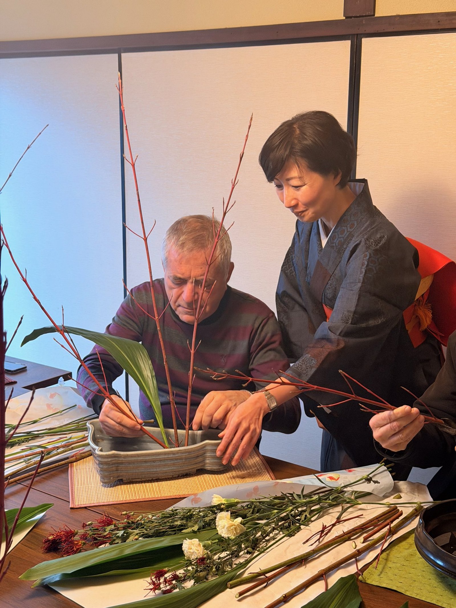An instructor helping a participant place branches in a shallow flower-arranging container.