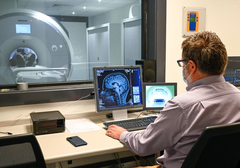 Photo from control room of technician looking at computer screen - with MRI scanner visible through the window