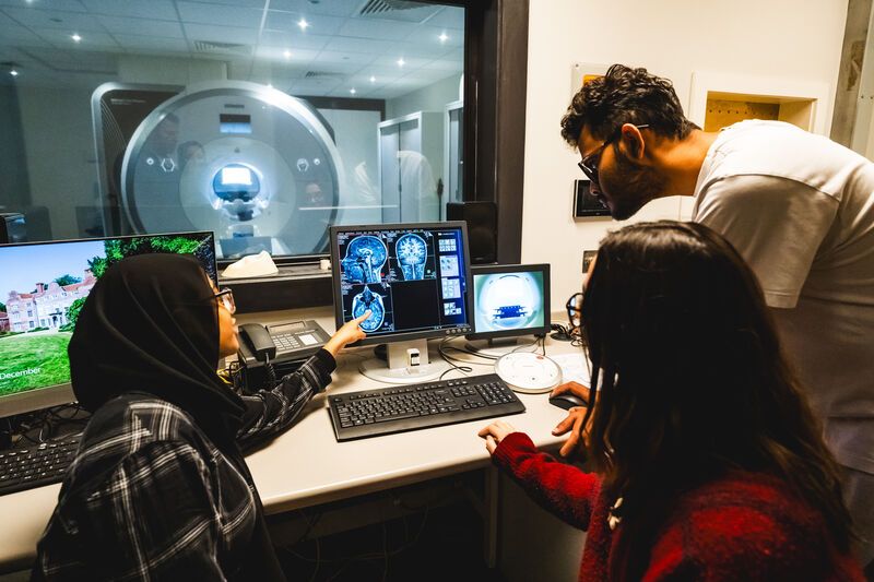 Photo from control room of researchers looking at computer screen - with MRI scanner visible through the window