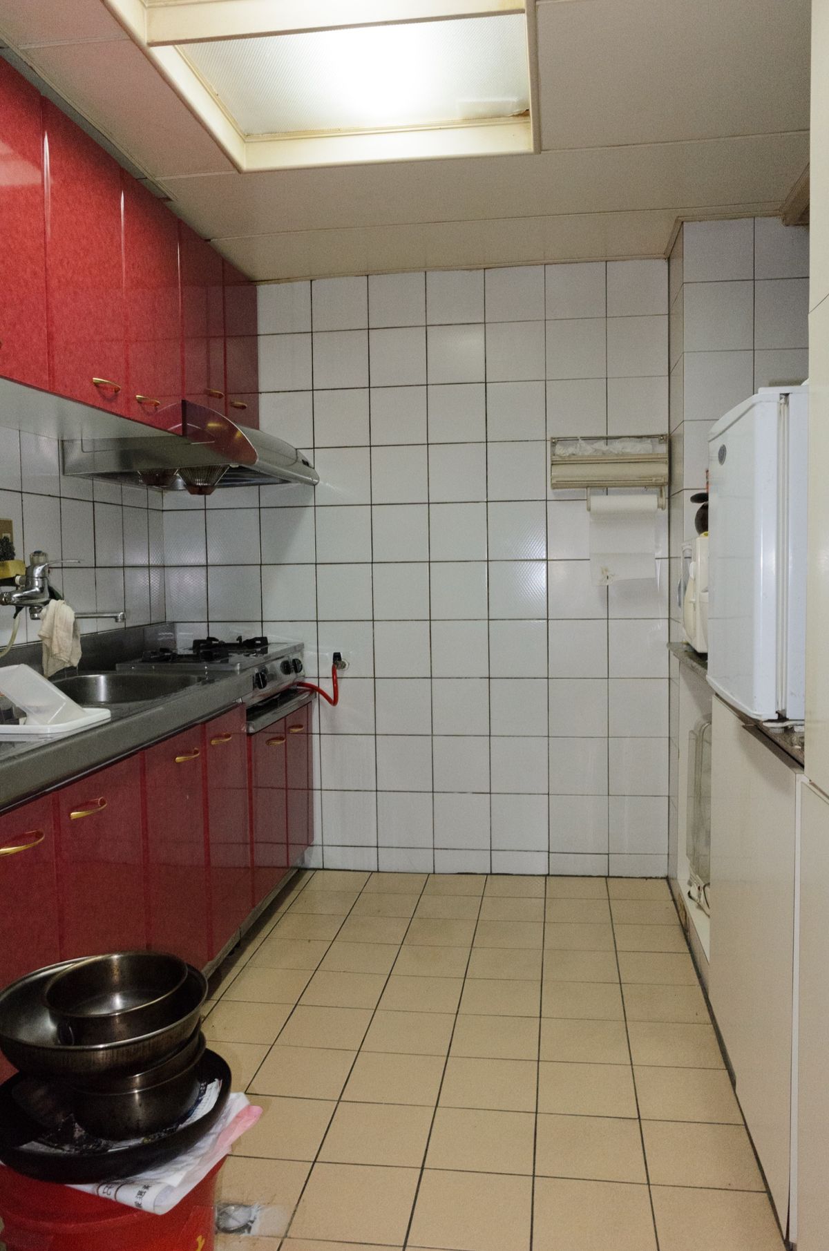 A tiled kitchen in an older Taipei apartment with red cabinets, a gas hob and a fridge