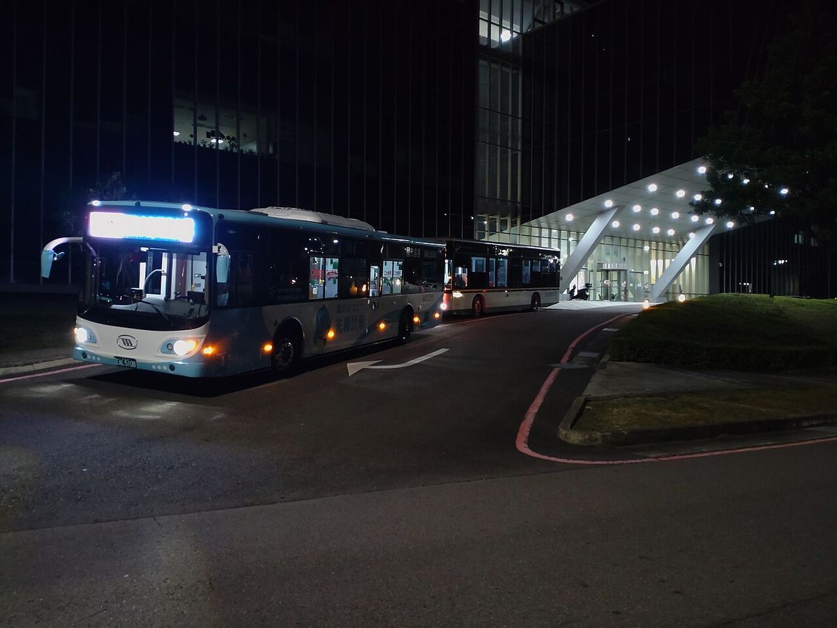 An orange Hsinchu Science Park shuttle bus parked next to a Hsinchu pilot electric bus
