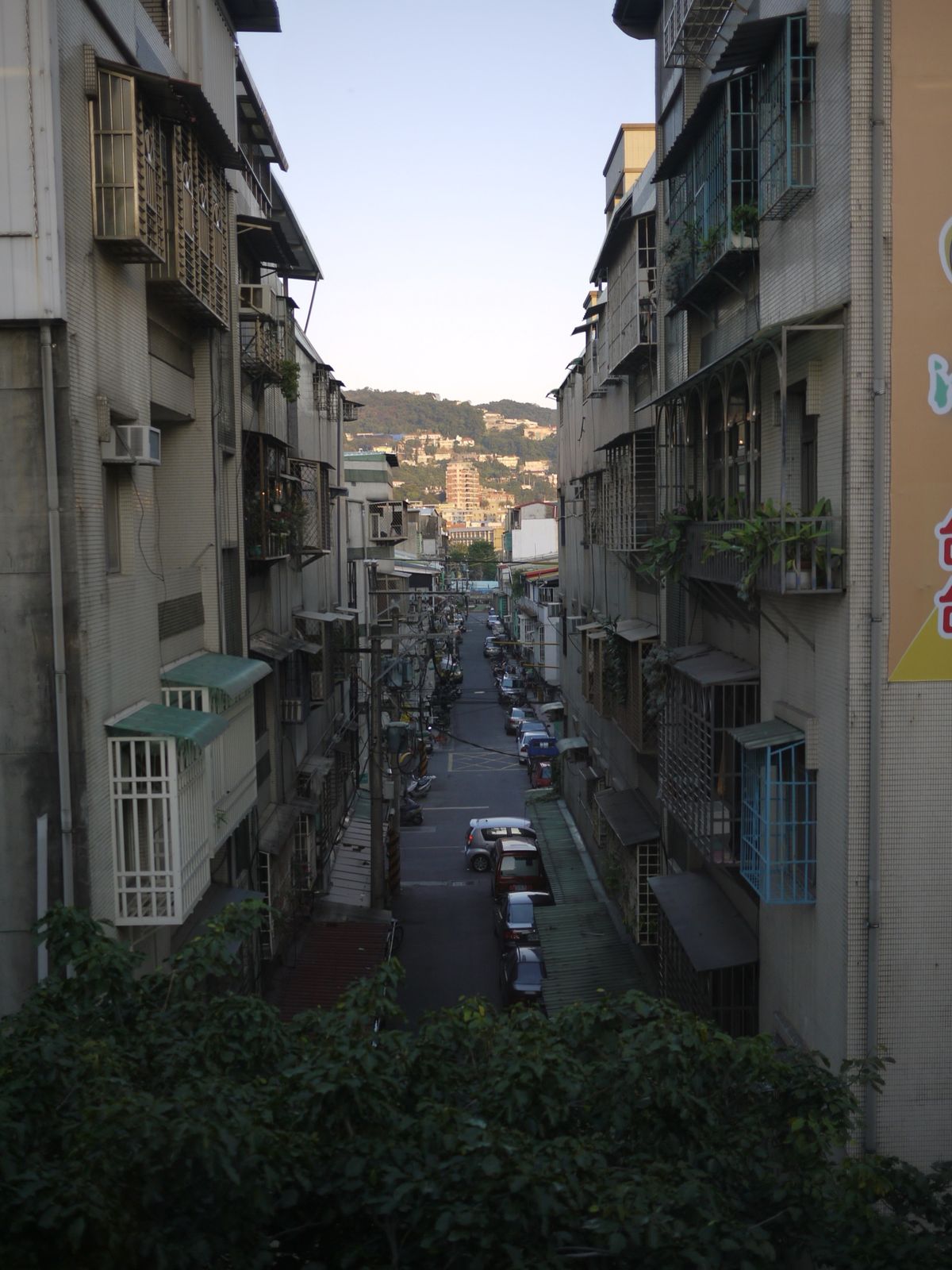 A narrow lane between older apartment buildings in Taipei, with the hills visible at the far end