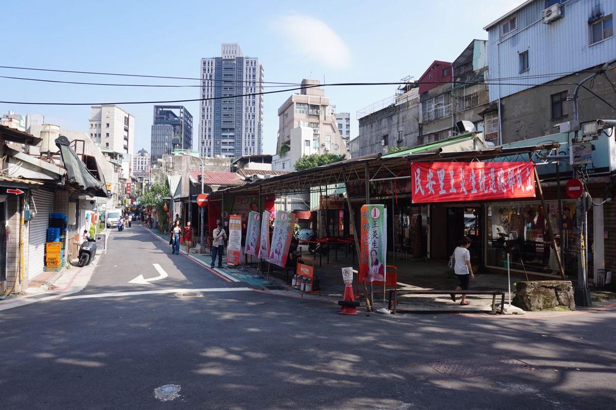 A sunny Zhongshan District street with older low-rise shops in front and newer high-rise apartment towers behind