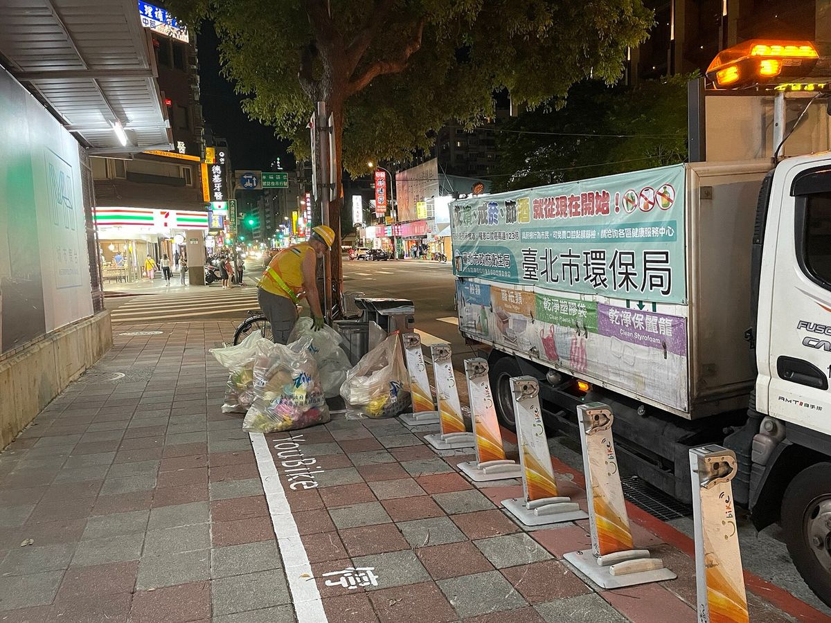 A Taipei Environmental Protection Department truck collecting bagged recycling from a sidewalk at night