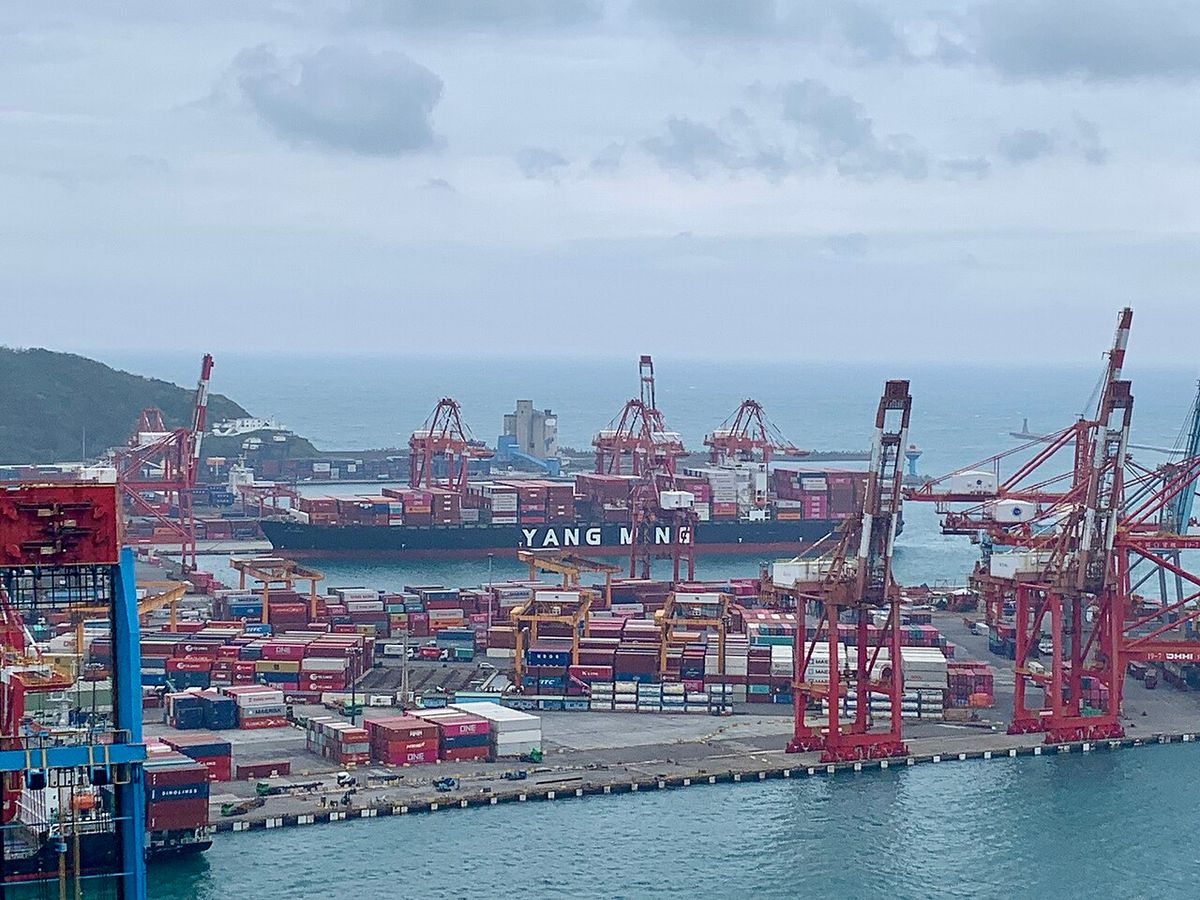 Container cranes and stacked shipping containers at the Port of Keelung, with a Yang Ming container ship docked
