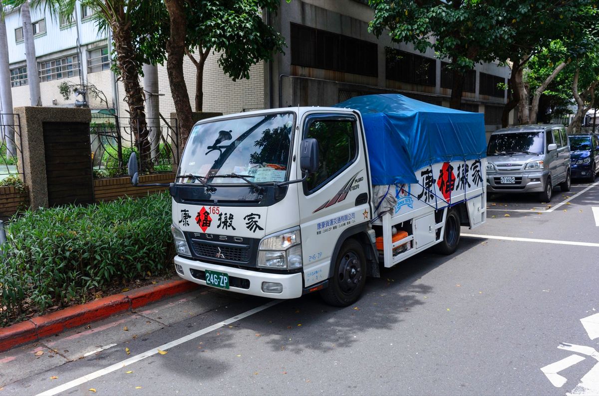 A moving company's truck parked on a tree-lined street in Taipei