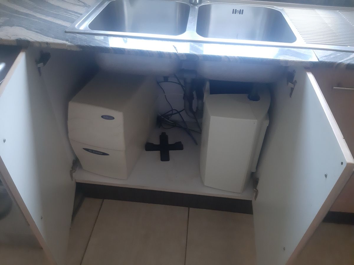 An under-sink water filter system installed in a kitchen cabinet below a double sink