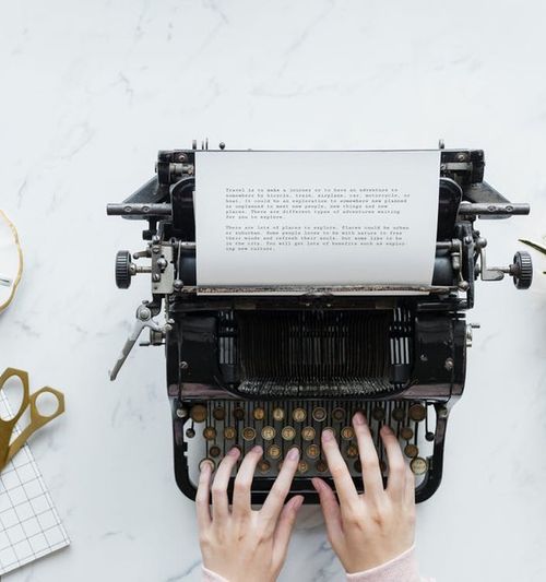 Image of a tabletop with a cup of tea and assorted items, female hands are seen typing on a typewriter