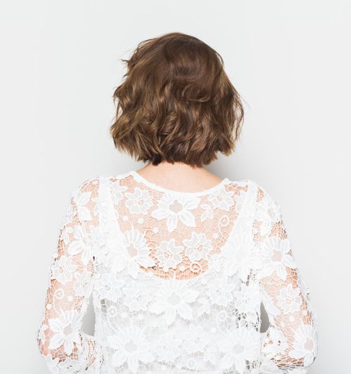 Image of a woman as seen from behind, wearing a white dress with lace flowers