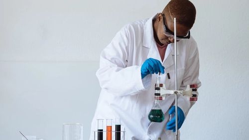 Scientist dressed in lab coat, adjusting a beaker full of fluid